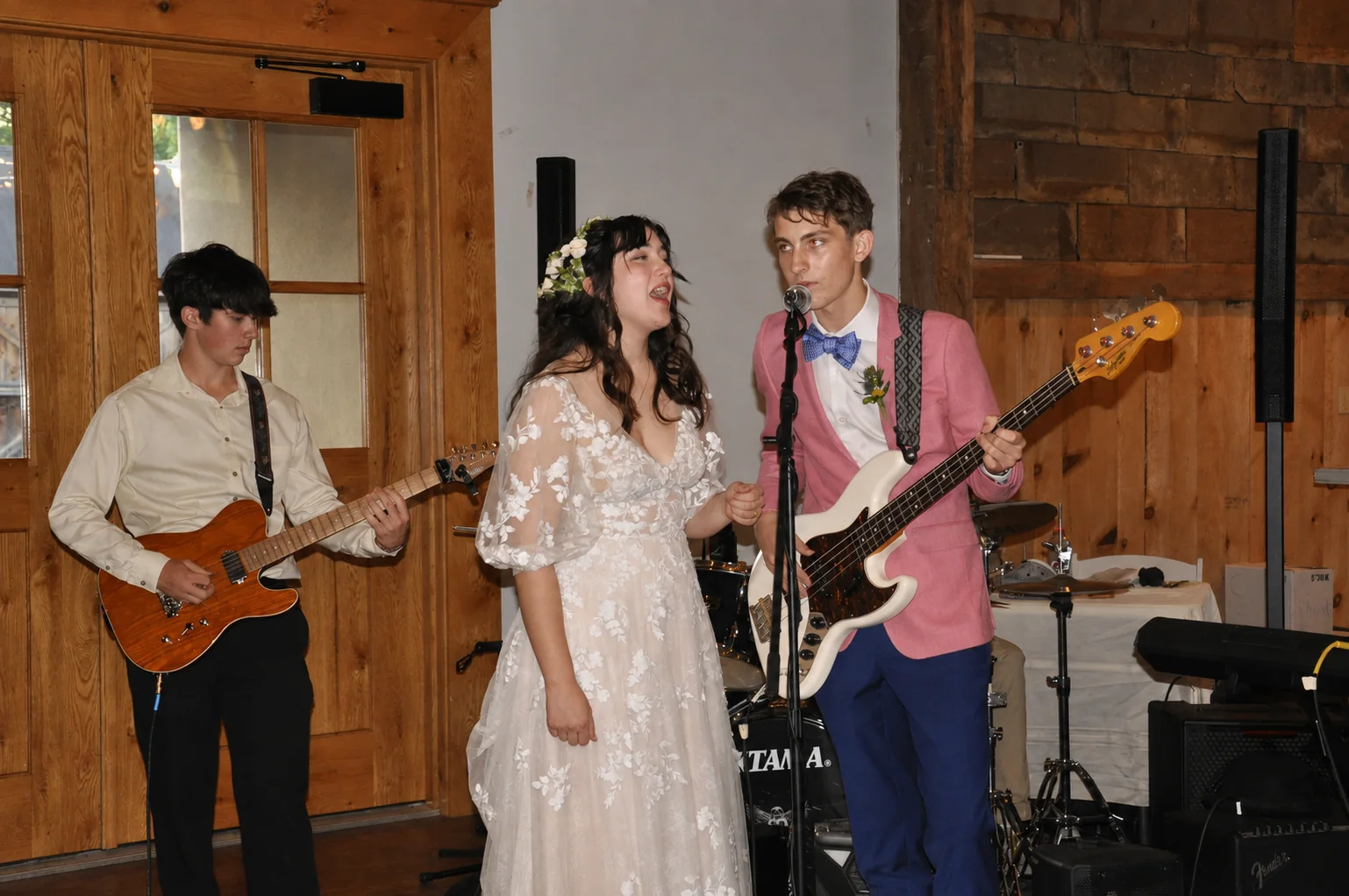 Bride singing beside her brother's band as he sings directly into a microphone at a wedding reception